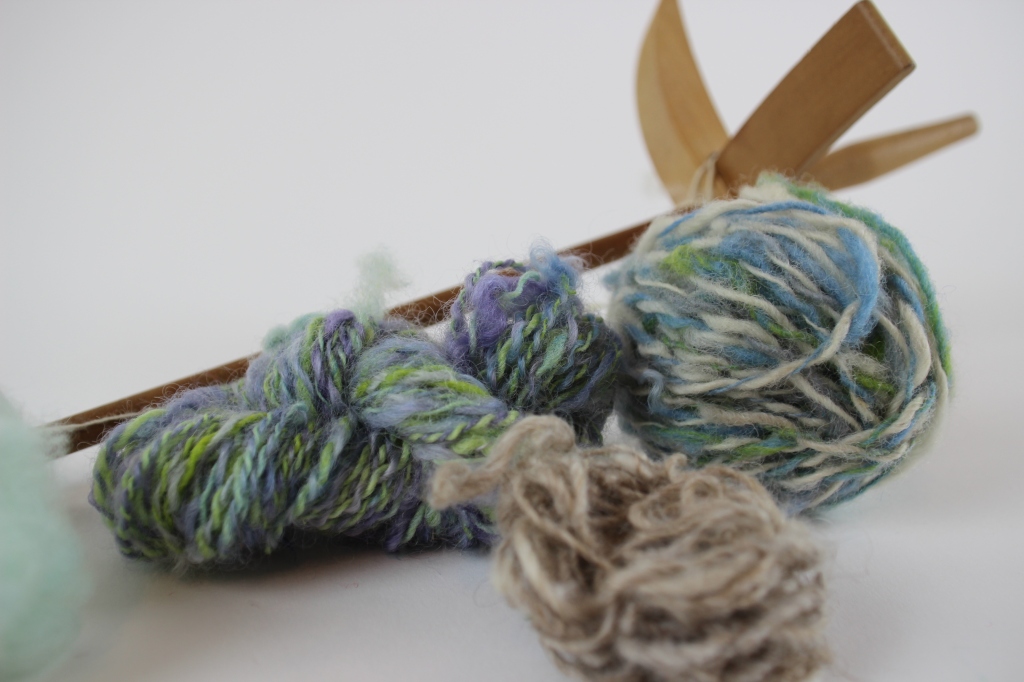 Hand spun yarn in green, blue and purple with a wooden drop spindle